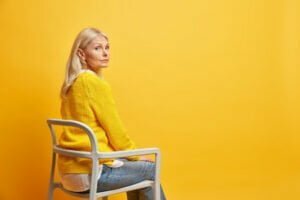 calm beautiful fifty years old woman sits chair being alone thinks about life wears yellow knitted sweater jeans blank copy space