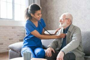 female attending physician holding stethoscope listening old patient during homecare visit