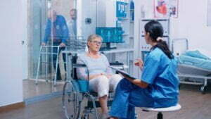 nurse talking with senior woman with walking disabilities sitting wheelchair into private modern recovery clinic hospital handicapped old retired patient medical consultation advice
