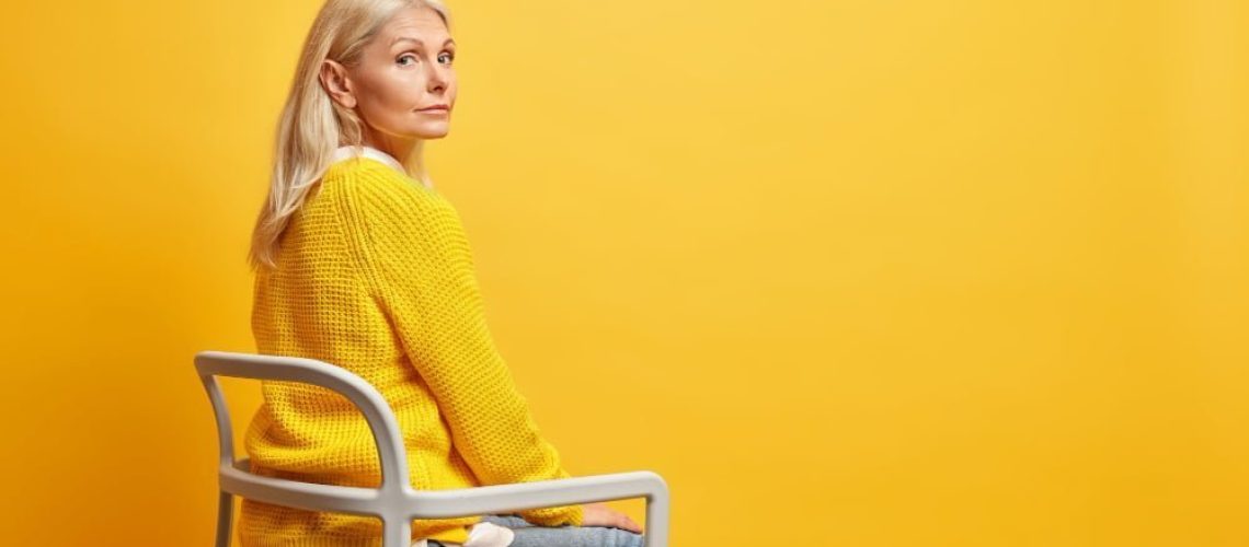 calm-beautiful-fifty-years-old-woman-sits-chair-being-alone-thinks-about-life-wears-yellow-knitted-sweater-jeans-blank-copy-space